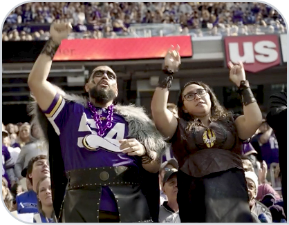 Fans dressed in Vikings gear cheer in the stadium stands.