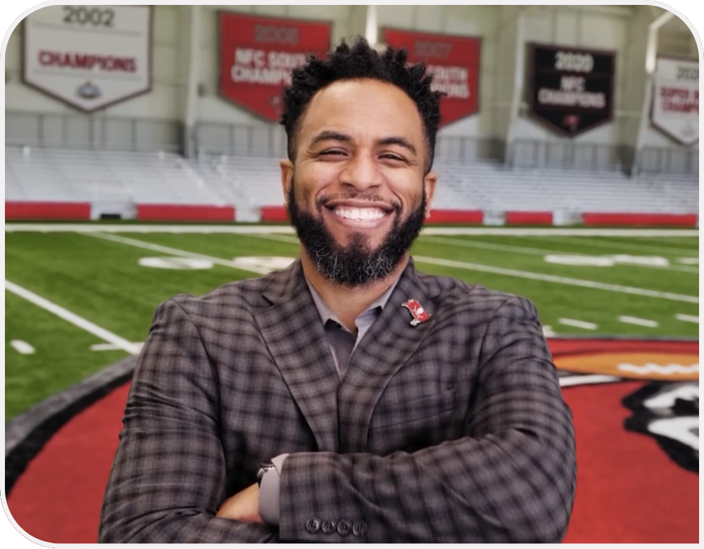 Charles Harris wears a blazer, smiles and stands on the field. 