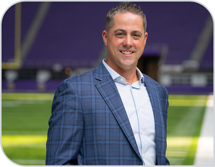 John Penhollow wears a suit and stands on the field. 