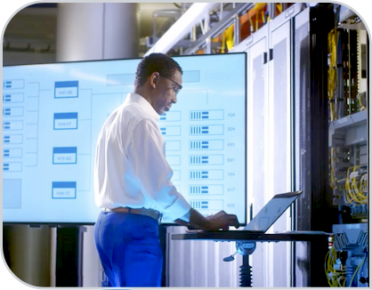 A businessperson works from a laptop in front of a large screen. 